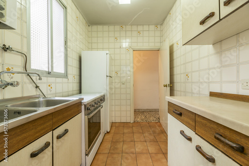 Old kitchen with old furniture in poor condition  white fridge  vintage tiles and aluminum window with translucent glass