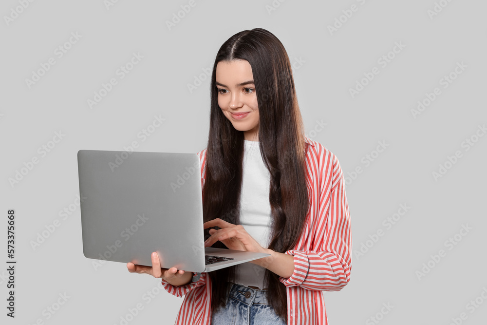 Naklejka premium Teenage girl with laptop on light grey background