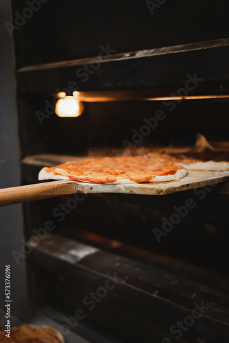 Baker man taking out freshly made pizza from oven with wooden shovel in bakery