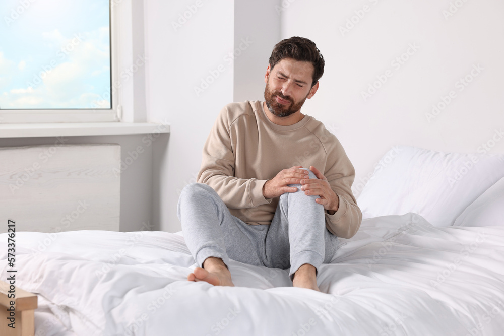 Man suffering from leg pain on bed at home Man suffering from leg pain on bed at home