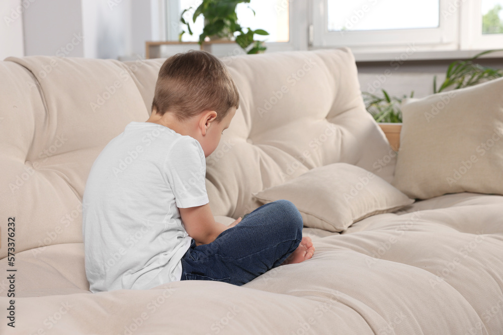 Boy with poor posture using phone on beige sofa in room. Symptom of scoliosis Boy with poor posture using phone on beige sofa in room. Symptom of scoliosis