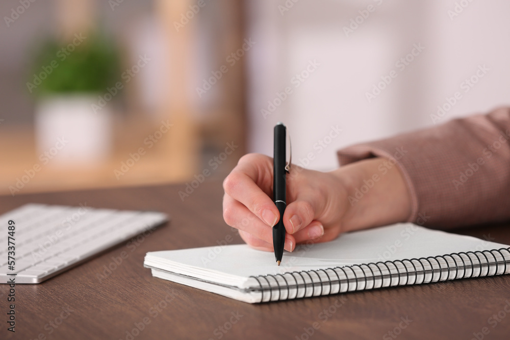 Fototapeta premium Woman writing in notebook at wooden table indoors, closeup. Space for text