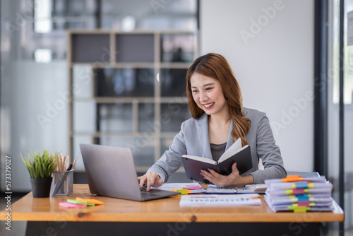 Young asian business woman manager accounting analyst checking bills, analyzing sales statistics management, taxes financial data documents or marketing report papers working in office using laptop.