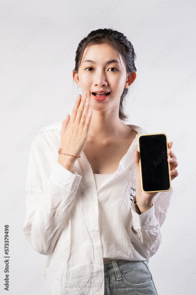 Attractive Young Asian woman pointing finger to mobile smartphone blank screen on isolated pink background.