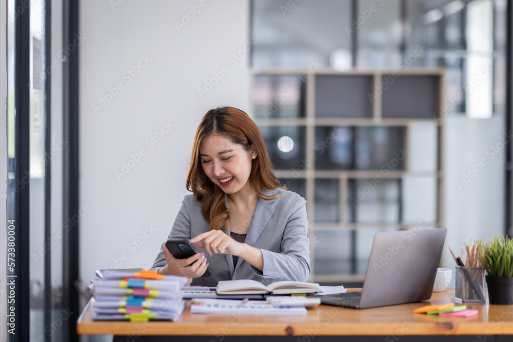Smiling young Asian business woman executive looking at smartphone using cellphone mobile cell tech, happy ethnic professional female worker working in office typing on cellphone sitting at desk. Smiling young Asian business woman executive looking at smartphone using cellphone mobile cell tech, happy ethnic professional female worker working in office typing on cellphone sitting at desk.