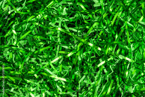 Easter grass, strips of green foil and lighter green paper, as a green background 