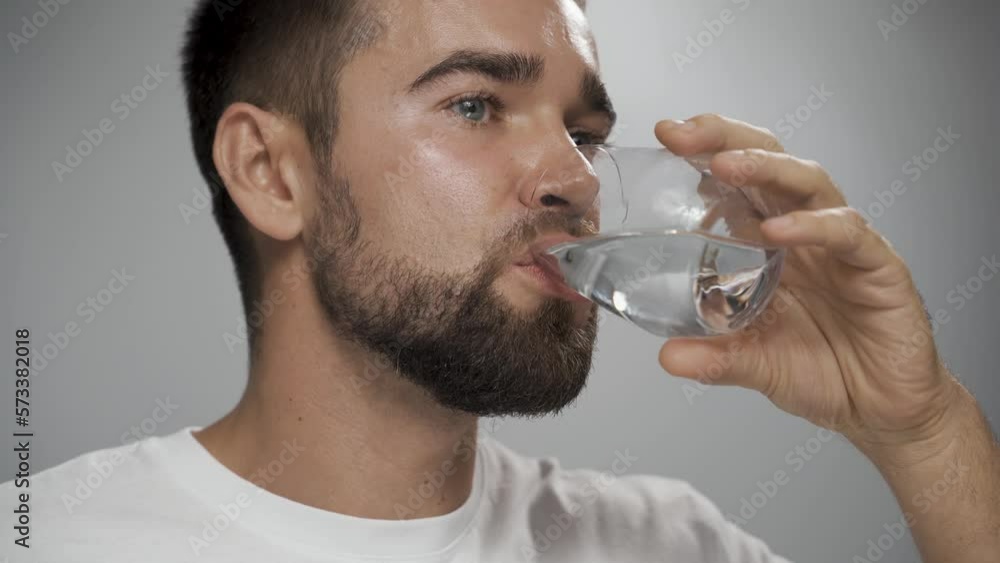 Handsome man drinking fresh water against gray background Handsome man drinking fresh water against gray background