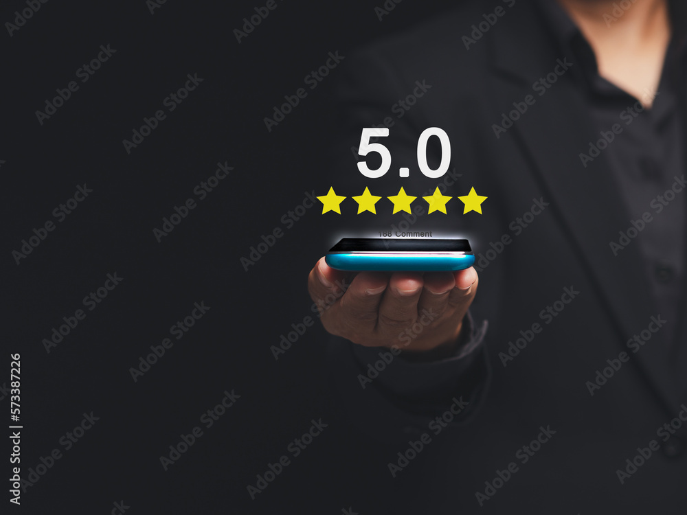 Satisfaction and feedback surveys. A businessman in a suit using a smartphone gives the five-star icon a rating of very impressed for service Satisfaction and feedback surveys. A businessman in a suit using a smartphone gives the five-star icon a rating of very impressed for service