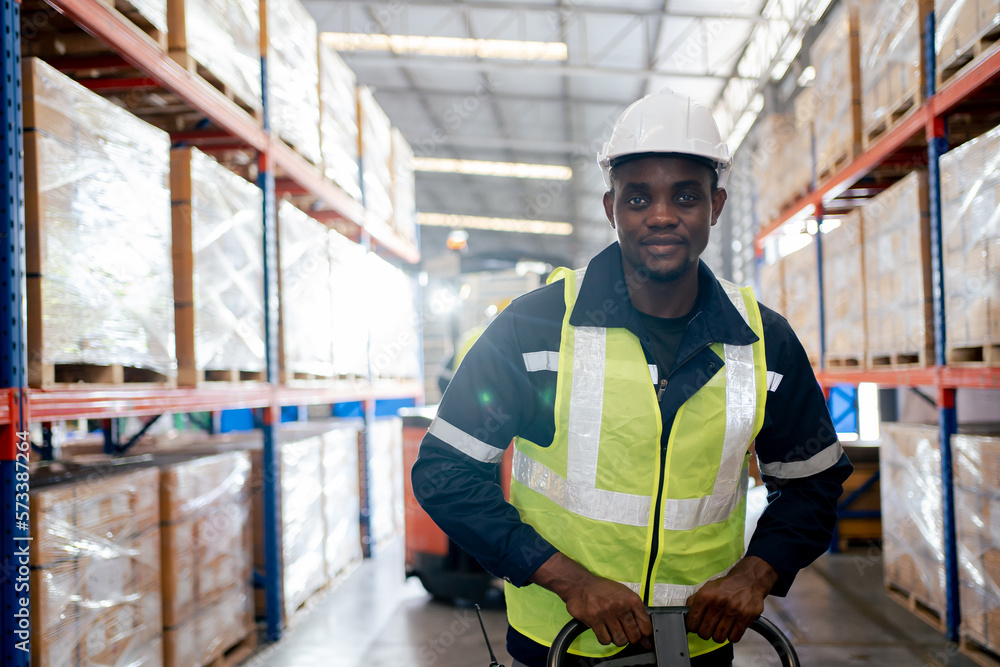 Professional Heavy Industry Engineer Worker Wearing Safety Uniform and Hard Hat. Smiling African American Industrial Specialist Walking in sparepart shelf in warehouse. Professional Heavy Industry Engineer Worker Wearing Safety Uniform and Hard Hat. Smiling African American Industrial Specialist Walking in sparepart shelf in warehouse.