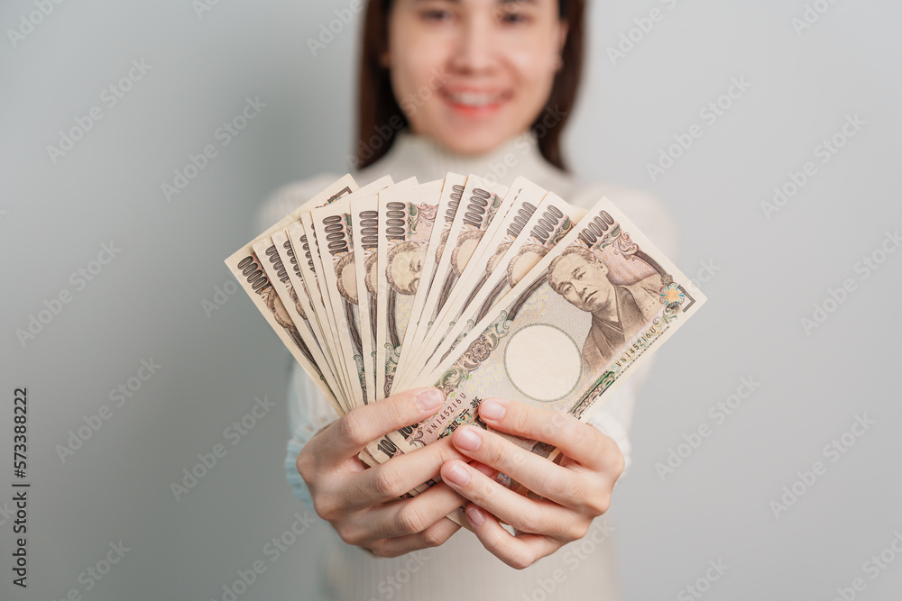 Woman hand holding Japanese Yen banknote stack. Thousand Yen money. Japan cash, Tax, Recession Economy, Inflation, Investment, finance and shopping payment concepts Woman hand holding Japanese Yen banknote stack. Thousand Yen money. Japan cash, Tax, Recession Economy, Inflation, Investment, finance and shopping payment concepts