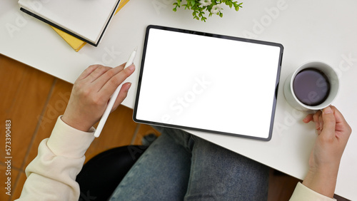 A female freelancer using digital tablet and sipping morning coffee at her modern office desk