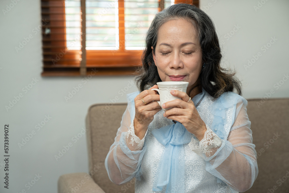 Foto de Happy Asian retired woman enjoying her morning tea in the house ...