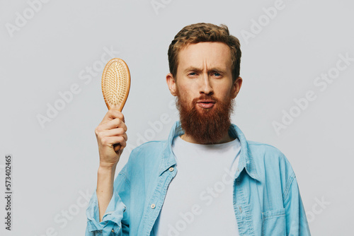Portrait of a man with a massage comb in his hands, combing his hair and beard, hair loss problem