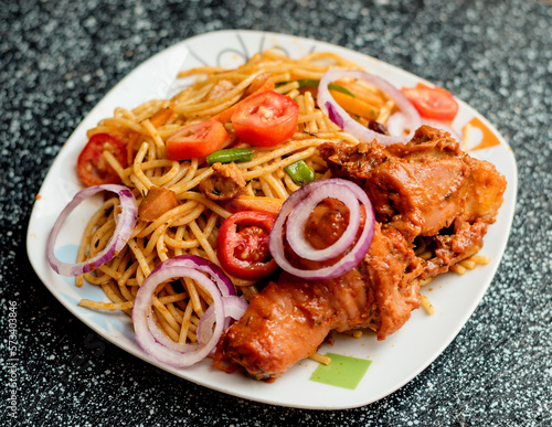 An assorted delicious dish of spaghetti noodles and chicken meat, garnished with sliced onions and tomatoes among other mouth watering food ingredients and spices cooked in Nigeria