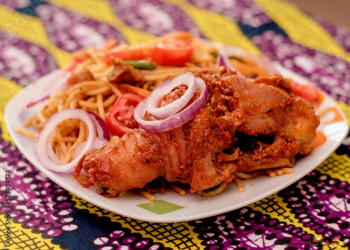 An assorted delicious dish of spaghetti noodles and chicken meat, garnished with sliced onions and tomatoes among other mouth watering food ingredients and spices cooked in Nigeria