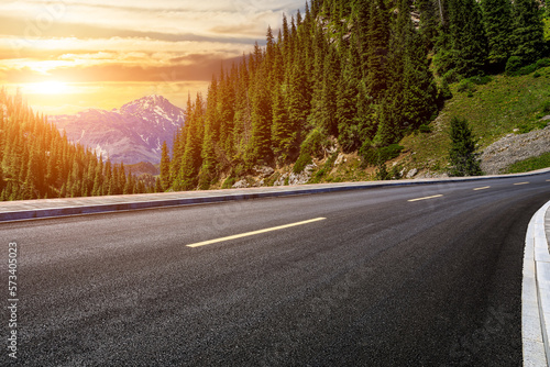 Asphalt road and green forest with mountain natural scenery at sunset in Xinjiang, China.