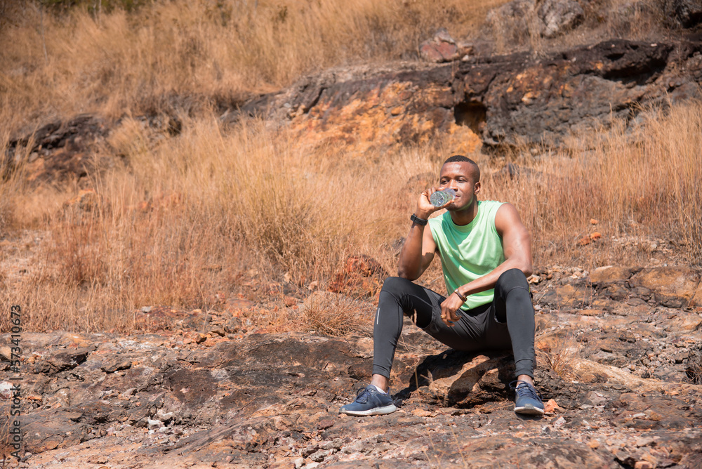 African American athletic man resting on the way sitting drinking water after running sport training outdoor in summer, workouts running and healthy lifestyle, sports and wellness.