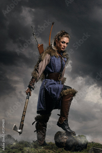 Beautiful female viking woman warrior in battle with ax and bow with arrows. Amazon fantasy blonde