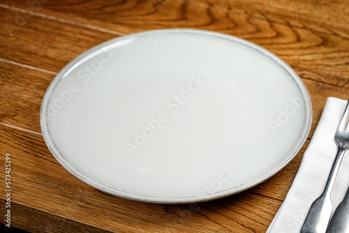 Empty grey plate with fork and knife on wooden table in restaurant. Mock up, template, display.