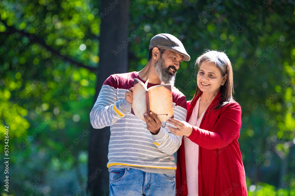 Obraz premium Senior Indian man and woman reading book at park.