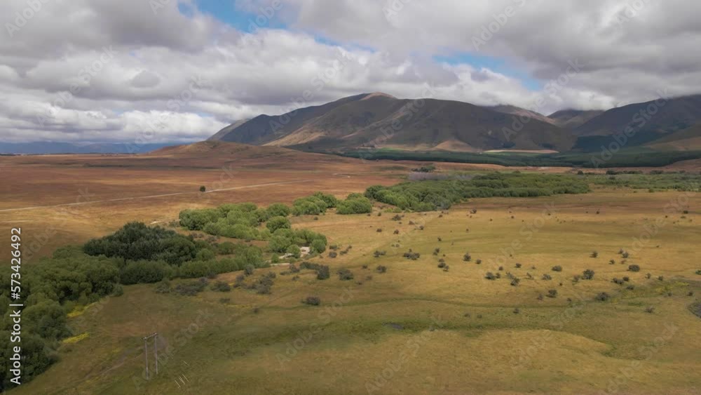 Curved drone flight over vast, wild landscape with lush tree line leading along river and towards mountain range Curved drone flight over vast, wild landscape with lush tree line leading along river and towards mountain range