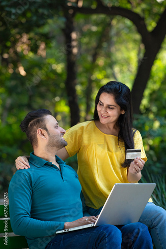 Indian man and woman using laptop and bank card at park. © PRASANNAPIX