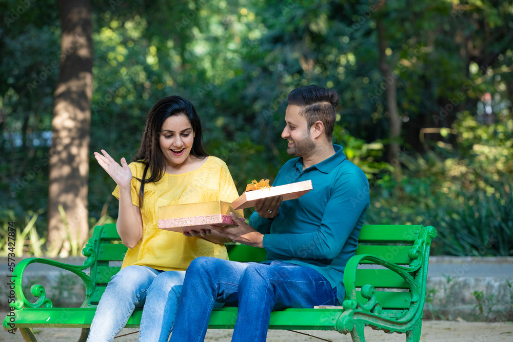 Fototapeta premium Young man giving surprise gift to young woman at park.