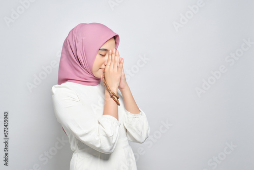 Young Asian Muslim woman praying to god with tasbih isolated over white background