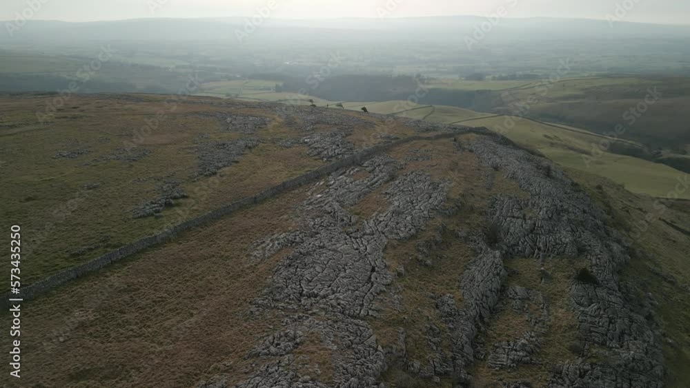 Flying over hillside and limestone pavement revealing green patchwork fields at Ingleton Yorkshire UK