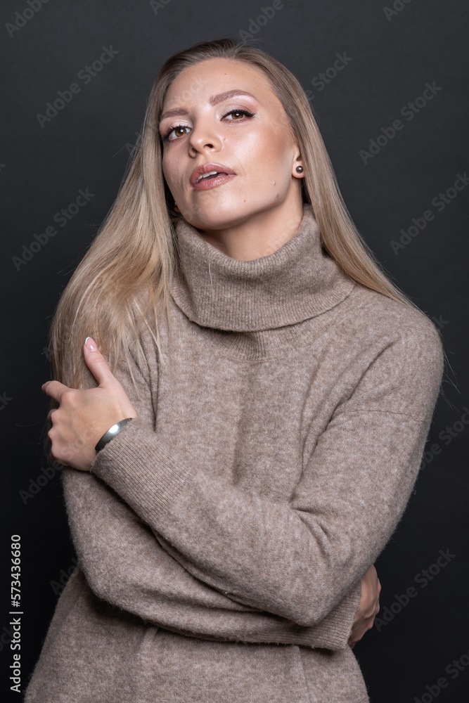 Studio portrait of beautiful brunette woman with day make-up and cozy beige sweater. Model hugging herself with hands and looking at the camera. Toned image with blue color Studio portrait of beautiful brunette woman with day make-up and cozy beige sweater. Model hugging herself with hands and looking at the camera. Toned image with blue color