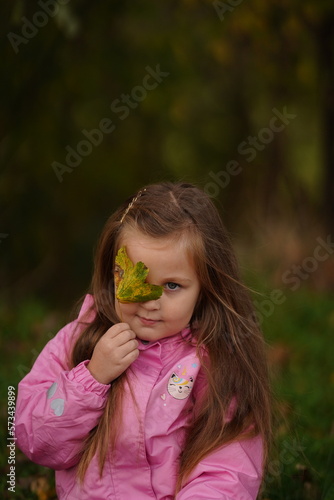 Little girl with yellow leaf. Child playing with autumn golden leaves. Kids play outdoors in the park. Children hiking in fall forest. Toddler kid under a maple tree on a sunny October day