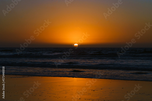 Golden sunset on the beach, tranquil scene. Sun setting down the horizon, ocean waves, and bright yellow sky on background © Hanna Tor