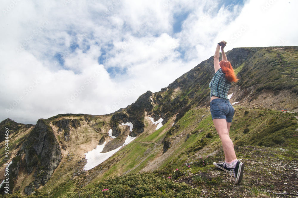 Mountain hiking scenic photography. Picture of female adventurer stretching arms upwards with cloudy sky on background. High quality wallpaper. Photo concept for ads, travel blog, magazine, article