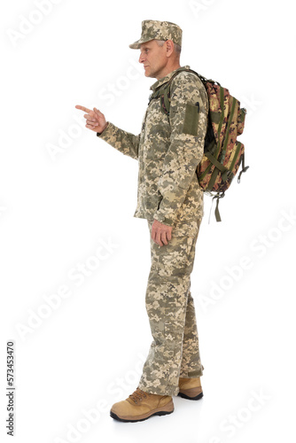 Side view full length portrait of old Ukrainian defender with backpack pointing to somebody. Ukraine army soldier posing in studio, isolated on white background. Stand for Ukraine.