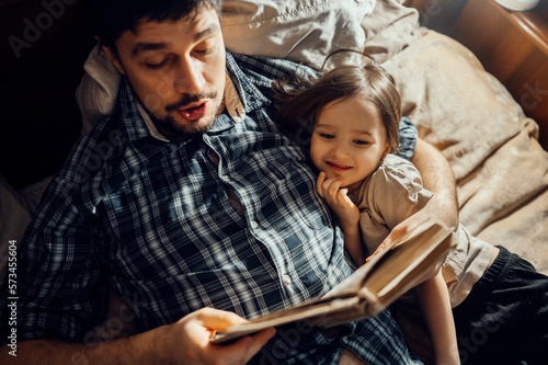 Father reading story book lying with son on bed