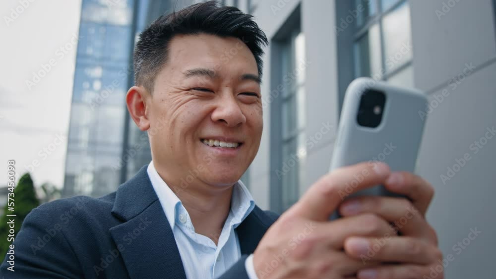 Closeup positive Asian Korean Chinese middle-aged 40s businessman adult man employer entrepreneur smile laugh browsing mobile phone chatting texting online business email in smartphone smiling in city Closeup positive Asian Korean Chinese middle-aged 40s businessman adult man employer entrepreneur smile laugh browsing mobile phone chatting texting online business email in smartphone smiling in city