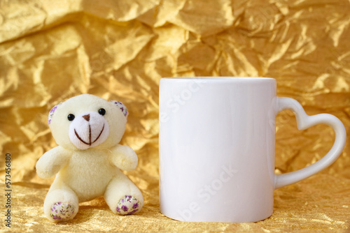 Mockup white blank mug with Teddy bear on golden background, copyspace. Template for your design. photo