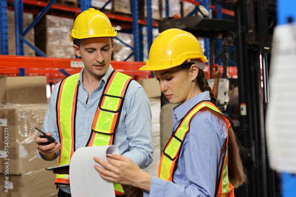 Group of warehouse workers with hardhats and reflective jackets using tablet, walkie talkie radio and cardboard while controlling stock and inventory in retail warehouse logistics, distribution center Group of warehouse workers with hardhats and reflective jackets using tablet, walkie talkie radio and cardboard while controlling stock and inventory in retail warehouse logistics, distribution center