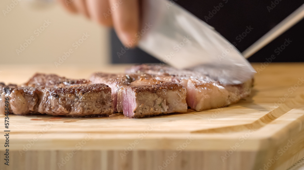 The close up image of a chef cutting medium rare grilled beef steak with chef knives on a wooden chopping board.