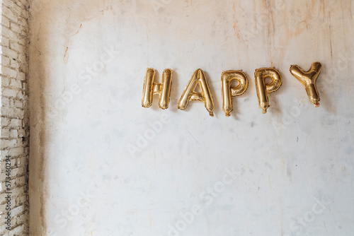 Gold colored happy text made with inflated balloons hanging on wall photo