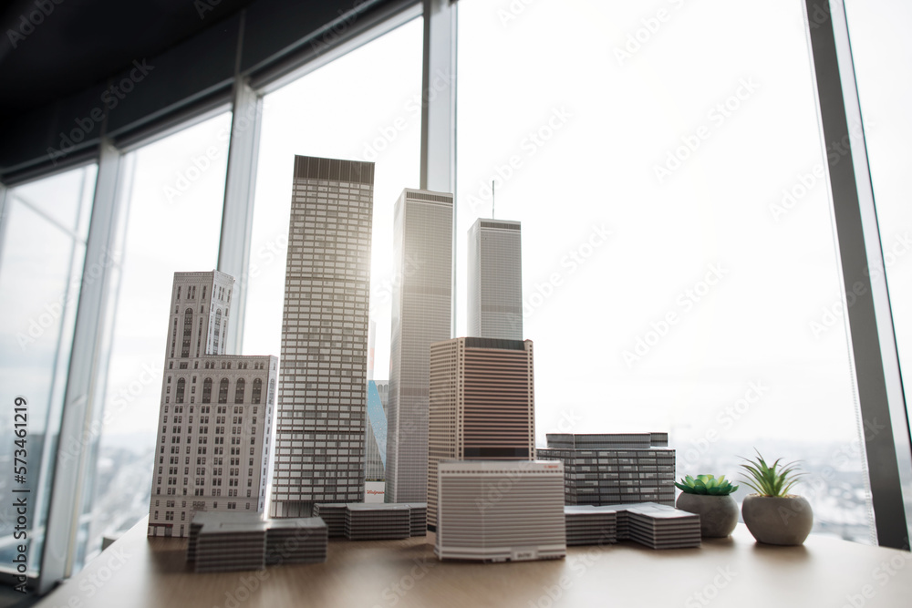 Fototapeta premium Architectural bureau office with panoramic windows and blurry cityscape. Building complex prototype project of residential or business district, city model. 3D city buildings on a wooden table.