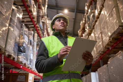 Low angle portrait of black woman wearing hardhat in storage warehouse and holding clipboard © Seventyfour