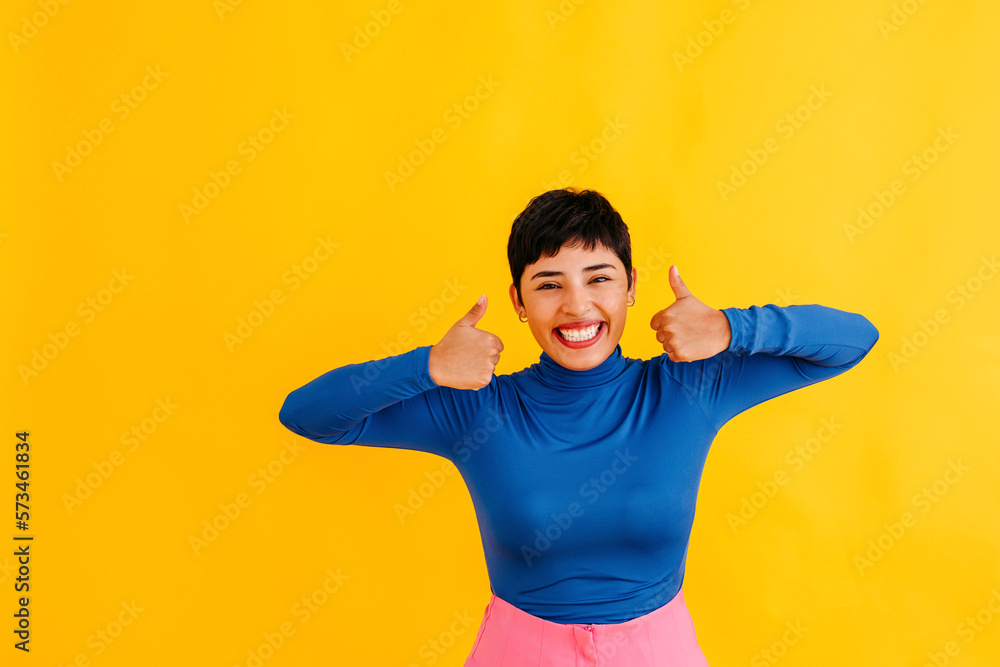 Happy young woman showing thumbs up against yellow background Happy young woman showing thumbs up against yellow background