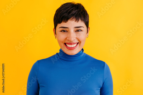 Happy young woman with pixie haircut standing against yellow background photo