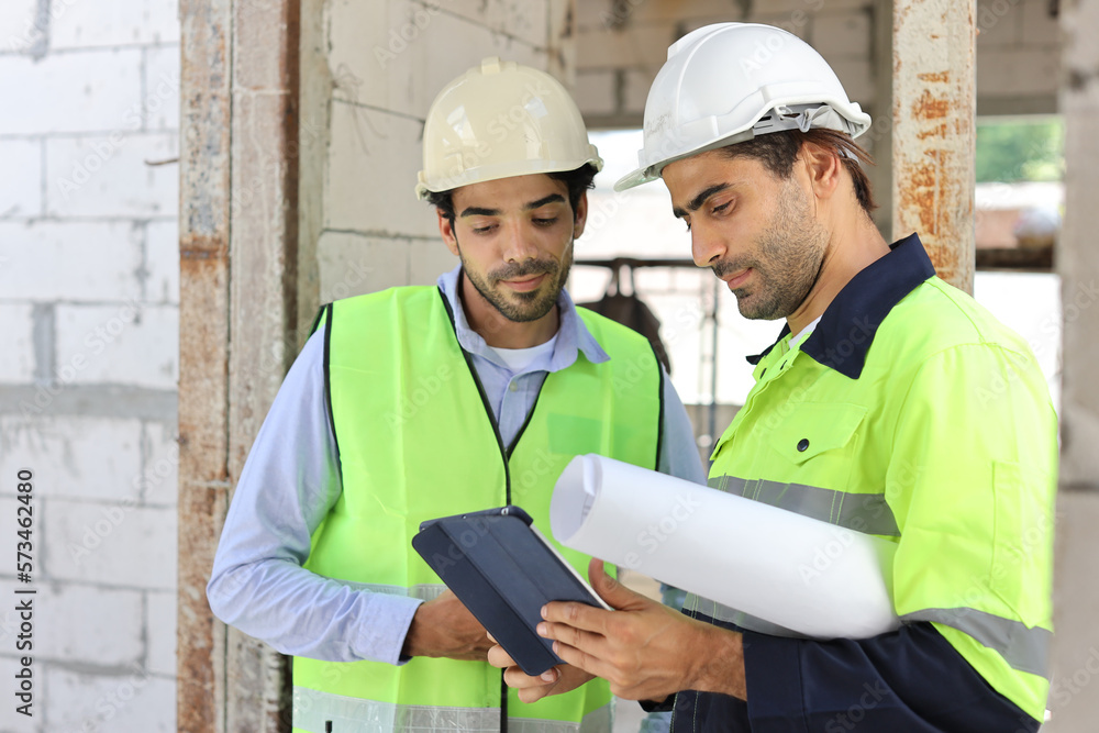 Two technician civil engineer or specialist inspector discussing, brainstorm and planing work with tablet, blueprint and walkie talkie radio together at Industrial building site. Construction concept Two technician civil engineer or specialist inspector discussing, brainstorm and planing work with tablet, blueprint and walkie talkie radio together at Industrial building site. Construction concept