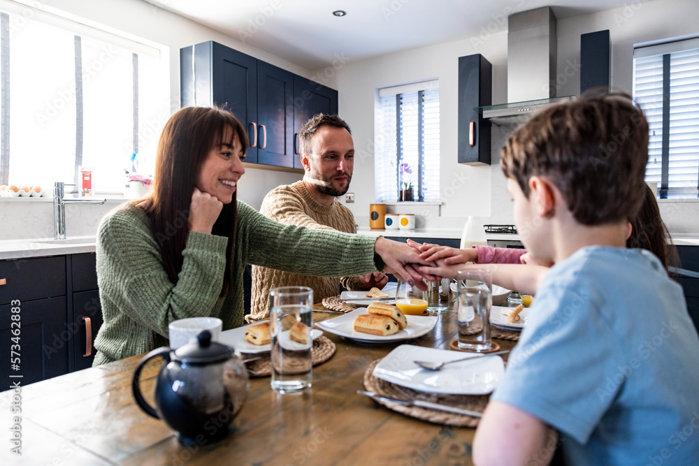 Happy family together enjoying breakfast with stacked hands at table Happy family together enjoying breakfast with stacked hands at table