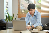 Pleasant young asian man communicating in social network, searching information online on laptop computer