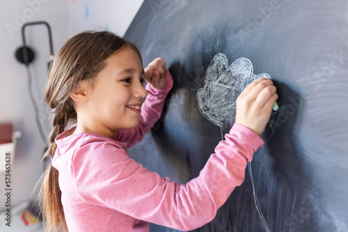 Happy girl drawing with chalk on board at home photo