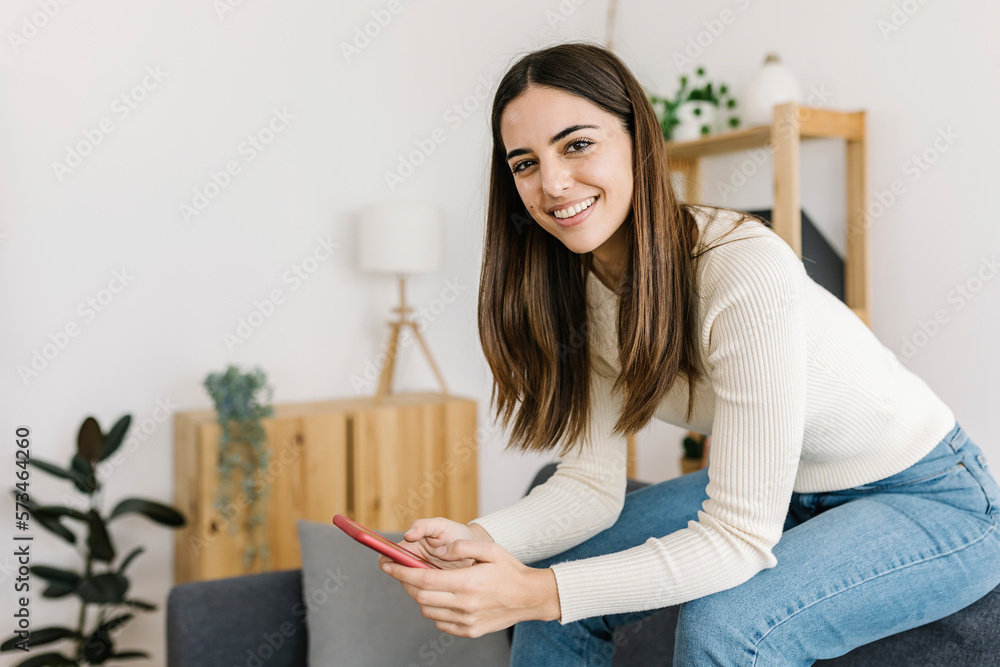 Smiling young woman sitting with smart phone at home Smiling young woman sitting with smart phone at home