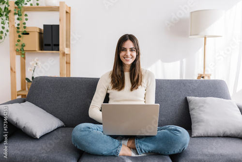 Smiling woman with laptop sitting cross-legged at home